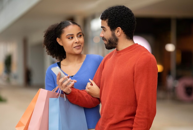 Coniugi misti che utilizzano l'applicazione per lo shopping mobile sul telefono nel centro commerciale