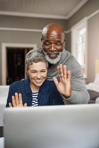 Connettiti con i tuoi cari ovunque tu sia Inquadratura di una coppia di anziani che saluta mentre usa un laptop a casa