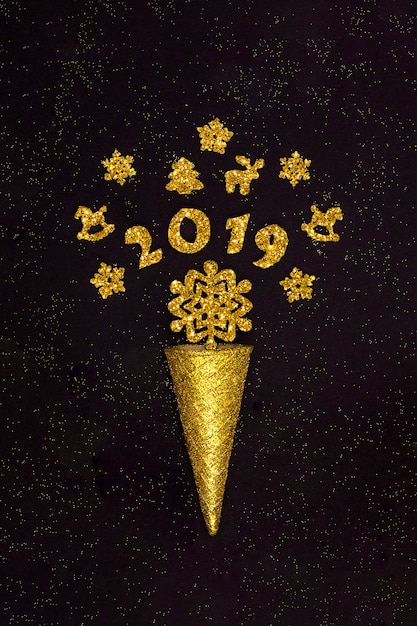 Cono di cialda d&#39;oro con figure 2019 e decorazioni natalizie, fiocchi di neve su fondo nero