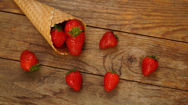 Cono gelato con fragole su uno sfondo di legno. Bacche rosse in un cono di cialda. Foto d'estate