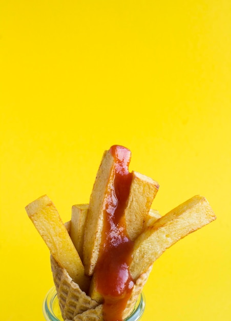 Cono gelato con patatine fritte e ketchup sullo sfondo giallo Closeup Copia spazio Posizione verticale