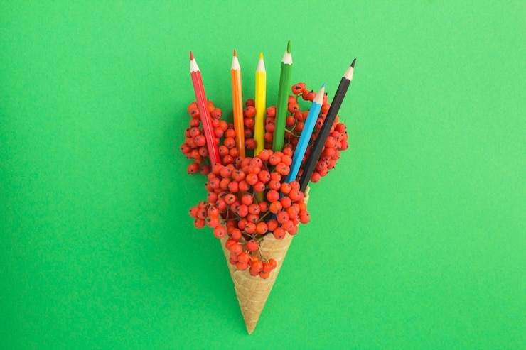 Foto cono gelato con sorba rossa e matite multicolori sulla superficie verde. vista dall'alto. copia spazio.