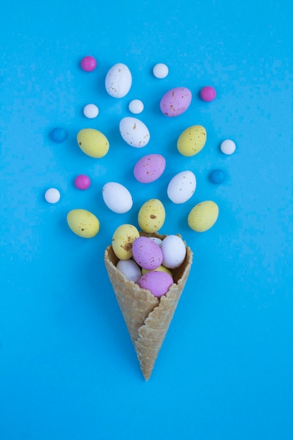 Cono gelato con uova di pasqua colorate su sfondo blu Vista dall'alto Copia spazio