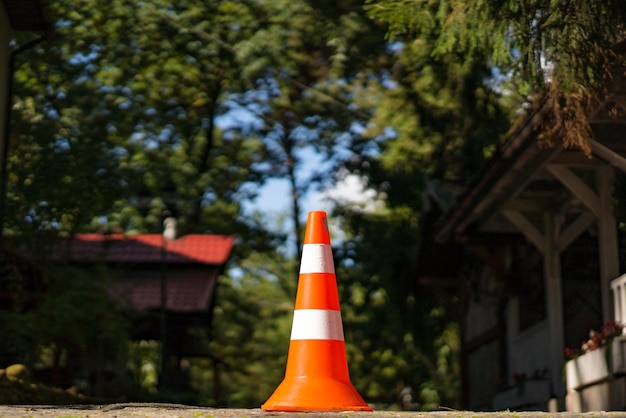 Cono stradale di due colori con arancione e bianco in piedi sullo sfondo naturale Cono di parcheggio arancione in plastica a strisce di avvertenza vicino alle case nella foresta