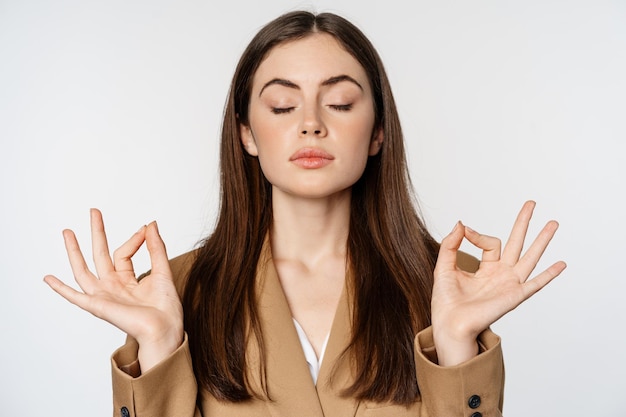 Consapevolezza e meditazione. Giovane imprenditrice meditando, pratica yoga, respirando calma e rilassata, in piedi su sfondo bianco