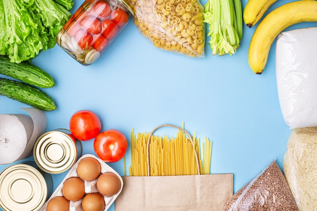 Consegna cibo. Riso, grano saraceno, pasta, conserve, zucchero, pomodori, cetrioli, banane su sfondo blu.