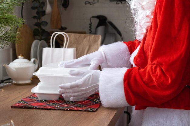 Consegna del cibo ai contenitori del servizio a domicilio nelle mani di Babbo Natale lo mette sul tavolo della cucina e lo porta via Ordine caldo pronto Natale Vacanze di capodanno catering