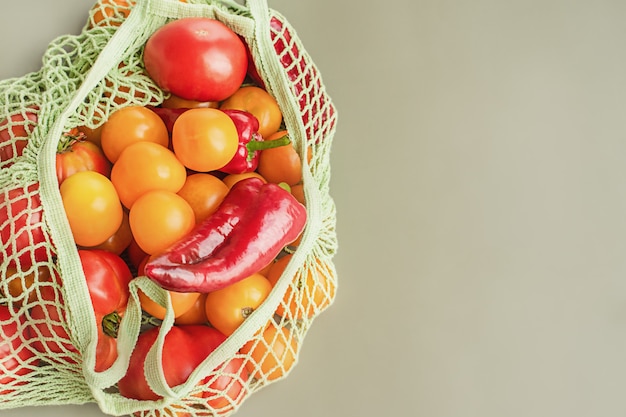 Consegna del cibo in borsa ecologica verde. Verdure pomodori e peperoni gialli e rossi in una griglia.