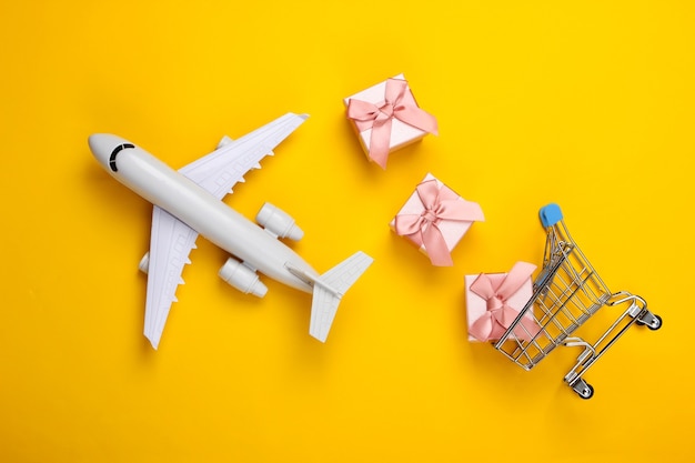 Consegna dell'aria. Statuetta di aereo, carrello della spesa e scatole regalo su giallo.