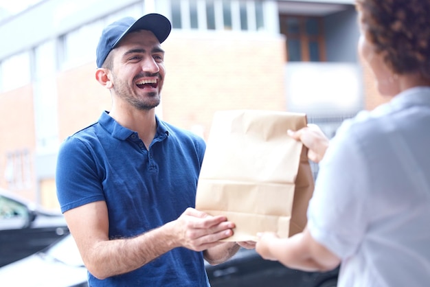 Consegna dell'uomo felice e sacchetto di carta in città per il servizio di corriere fast food o shopping online alla porta Persona di sesso maschile che consegna un pacco o un ordine al cliente per la logistica dei trasporti o l'e-commerce