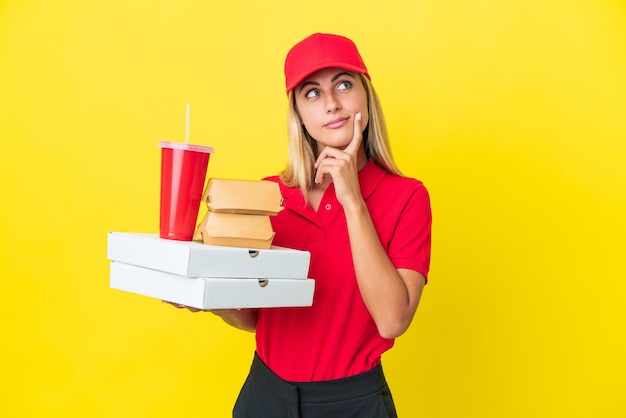 Consegna donna uruguaiana che tiene fast food isolato su sfondo giallo avendo dubbi mentre guarda in alto