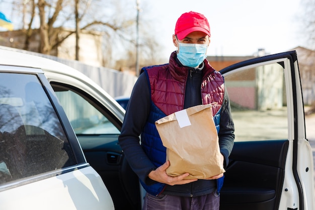 consegna in auto. uomo in maschera protettiva e guanti medici che tengono una scatola di carta. Servizio di consegna in quarantena, focolaio di malattia, condizioni di pandemia di coronavirus covid-19.