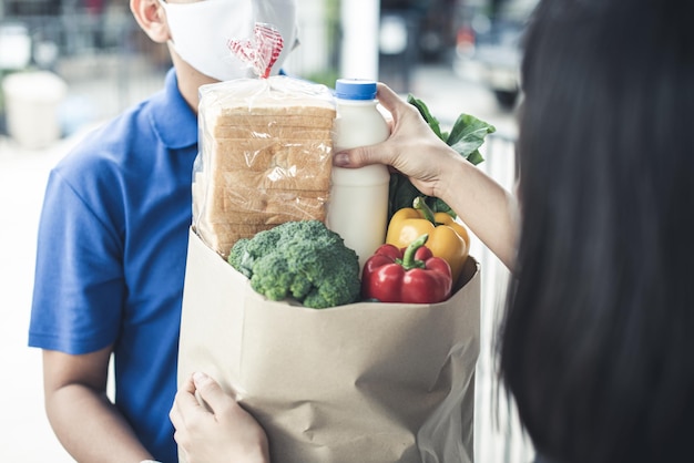 Consegna L'uomo asiatico indossa una maschera protettiva in uniforme blu e pronto per l'invio della consegna del sacchetto di cibo