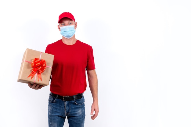 Consegna sicura di regali per le vacanze. Un corriere in uniforme rossa e maschera medica tiene la scatola. Banner.