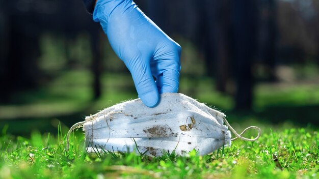 Consegnare il guanto medico raccogliendo una maschera medica sporca dall'erba