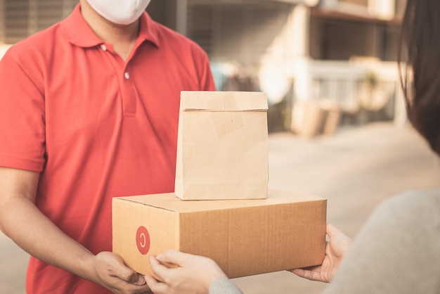 Consegnare l'uomo che indossa una maschera per il viso in una borsa per la manipolazione dell'uniforme rossa e una scatola per i pacchi regalare alla cliente femminile