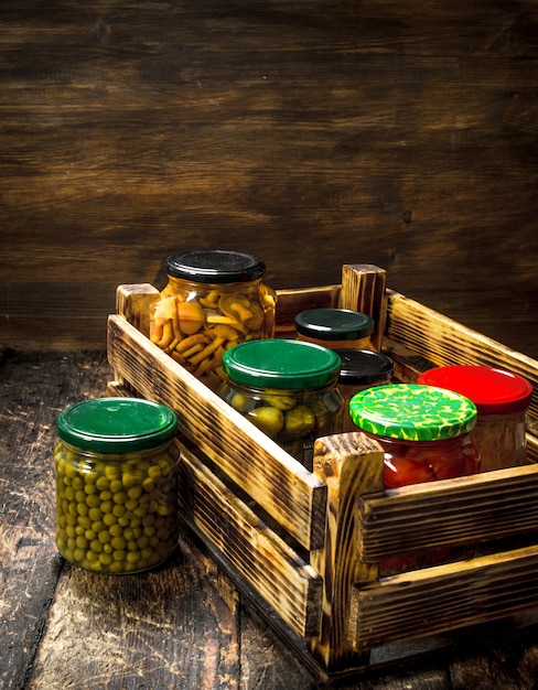 Conserva funghi e verdure in una scatola sul tavolo di legno.