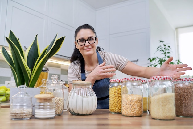 Conservare il cibo in cucina donna con vasetti e contenitori parlando e guardando la fotocamera