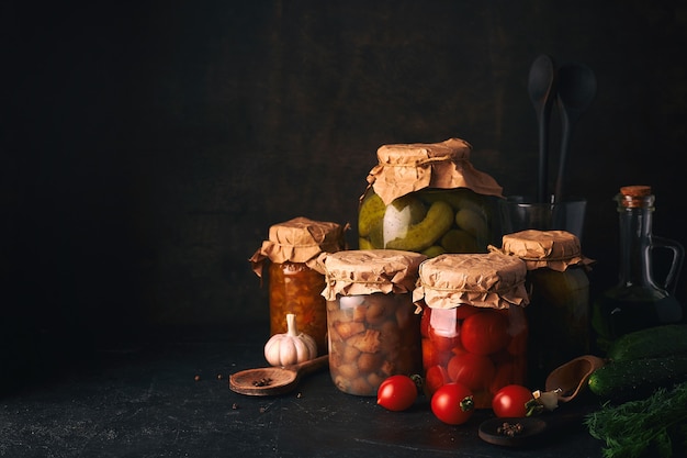 Conserve di frutta e verdura. Vasetti di vetro con verdure e frutta fermentate, in salamoia e in scatola sul tavolo da cucina rustico scuro. Copia spazio.