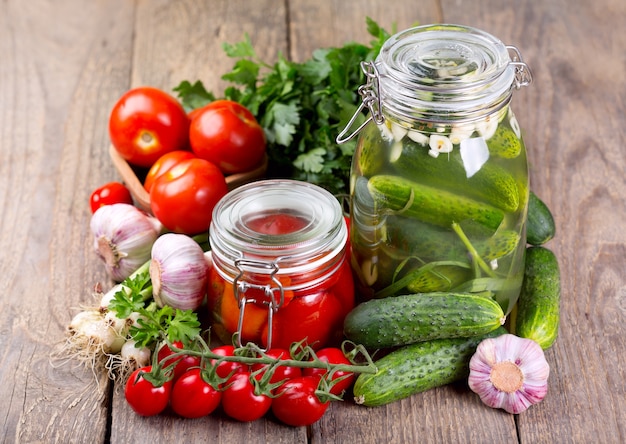 Conserve di pomodori e cetrioli con verdure fresche su un tavolo di legno