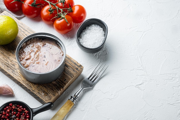 Conserve di tonno alalunga selvatico, su tagliere di legno, su sfondo bianco con erbe e ingredienti, con copyspace e spazio per il testo