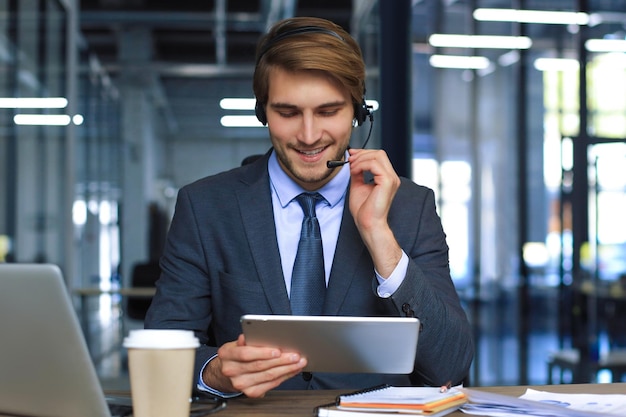 Consulente aziendale maschio sorridente con le cuffie seduto alla videochiamata dell'ufficio moderno guardando lo schermo del laptop L'agente del servizio clienti uomo dell'assistenza telefonica che parla chat online