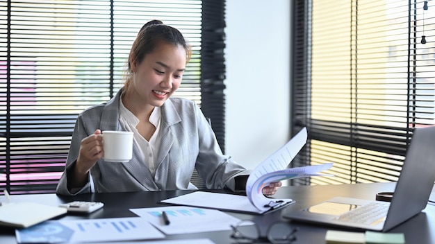 Consulente contabile femminile sorridente che controlla i rapporti finanziari sul suo posto di lavoro