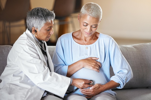 Consulenza sanitaria e donna incinta con medico sul divano per il controllo dell'esame e la salute del bambino durante la visita a casa Gravidanza della donna anziana e professionista medico che fa esame su paziente felice