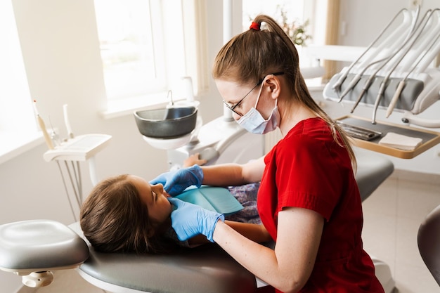 Consultazione con il dentista pediatrico in odontoiatria Il dentista pediatrico esamina i denti della bambina per il trattamento del mal di denti Dolore ai denti nei bambini