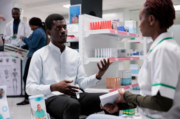 Consultazione del farmacista, venditore di farmacia e conversazione con il cliente, pillole di consulenza medica. Uomo afroamericano che prende medicinali, farmacia e comunicazione con il cliente, tutta la squadra nera