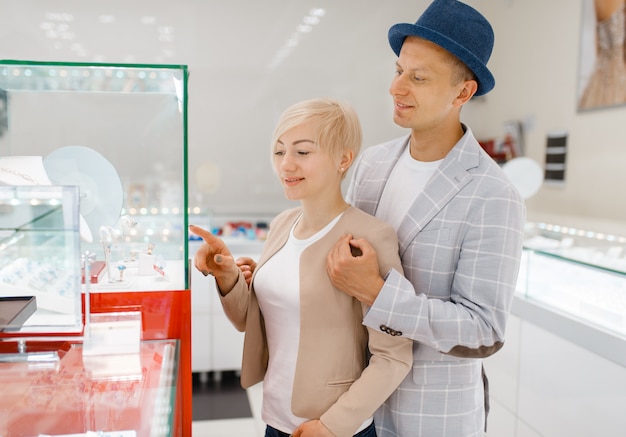 Consumatori di sesso maschile e femminile alla ricerca di gioielli in gioielleria. Uomo e donna che scelgono le fedi nuziali. Futuri sposi in gioielleria. Coppie di amore che acquistano decorazioni in oro