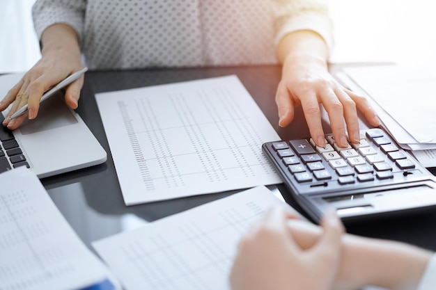 Contabilista donna che usa una calcolatrice e un computer portatile mentre conta le tasse con un cliente o un collega.