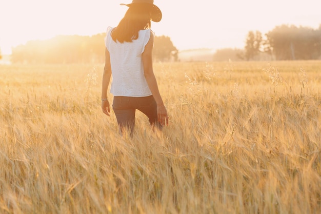 Contadina in cappello da cowboy che cammina con le mani sulle orecchie al campo agricolo al tramonto