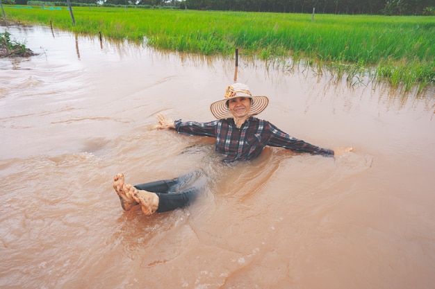 Contadino che gioca e si rallegra in una forte alluvione nel campo di riso di campagna o campagna