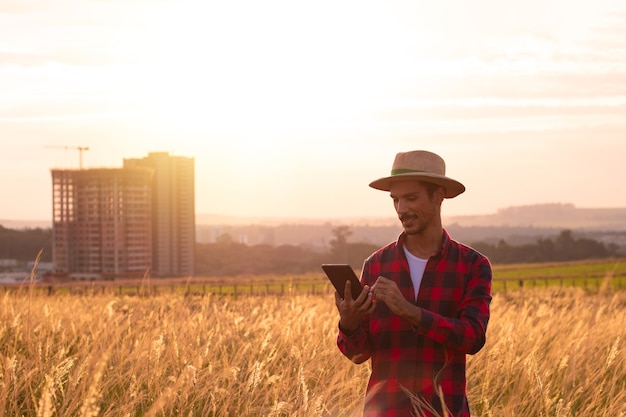 Contadino con cappello e tablet mobile che analizza la piantagione al tramonto.