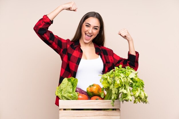 Contadino con verdure appena raccolte in una scatola isolata su sfondo beige che celebra una vittoria