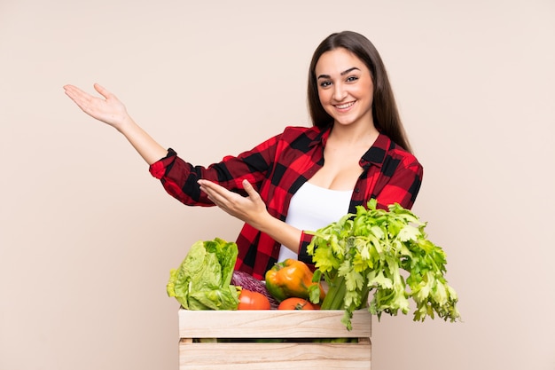 Contadino con verdure appena raccolte in una scatola su mani beige che si estendono a lato per invitare a venire