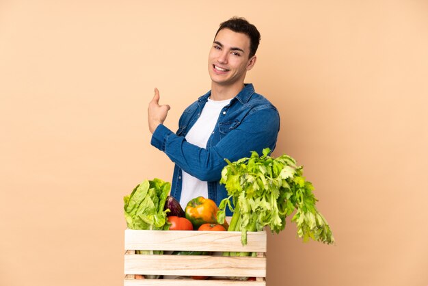 Contadino con verdure appena raccolte in una scatola sul muro beige che punta indietro