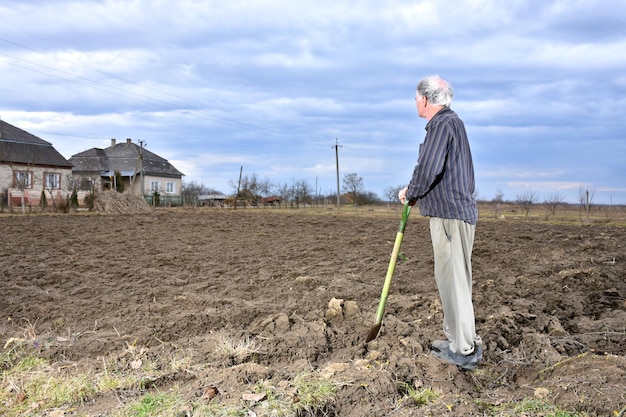 Contadino in piedi con una pala sul campo. Tempo di primavera. Inizio lavori di primavera sul campo