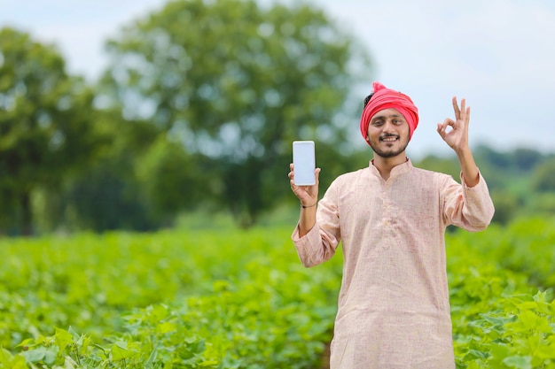 Contadino indiano che mostra lo schermo dello smartphone nel campo agricolo