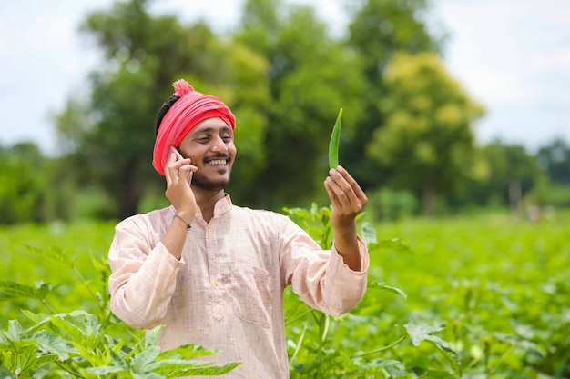 Contadino indiano che parla su smartphone al campo agricolo.