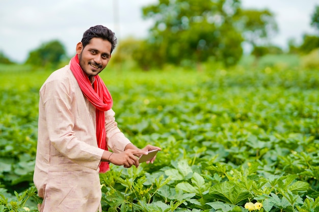 Contadino indiano che utilizza smartphone al campo agricolo.