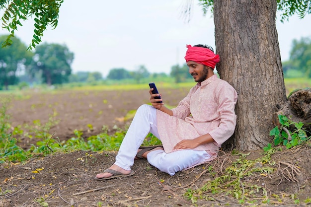 Contadino indiano seduto al campo agricolo e utilizza lo smartphone.