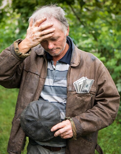 Contadino stressato con soldi in giacca su sfondo naturale