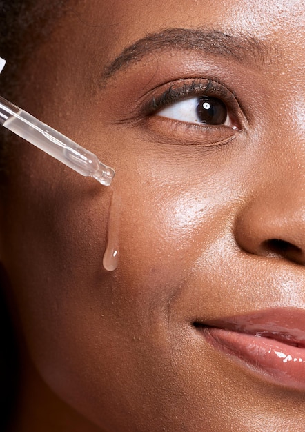 Contagocce donna nera e cosmetici per la cura della pelle del viso per l'idratazione della bellezza o il trattamento dell'olio per un viso sano Primo piano di una donna afroamericana che applica il siero sulla guancia per idratare la pelle