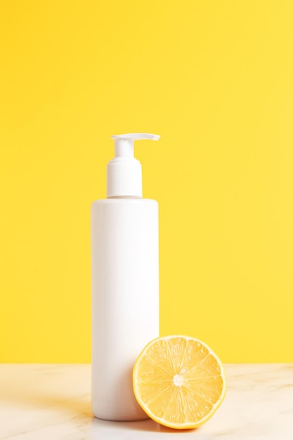 Contenitore cosmetico bianco e limone fresco su sfondo giallo Etichetta vuota per mockup di branding Concetto di prodotto di bellezza naturale Shampoo con crema di sapone gel doccia