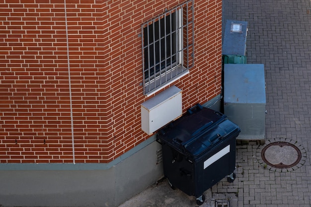 Contenitore della spazzatura nero in piedi vicino al muro della casa