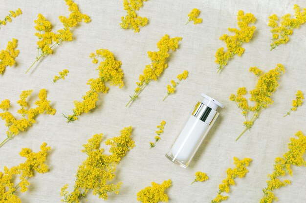 Contenitore di bottiglie cosmetiche e erbe gialle intorno a fiori freschi di campo bianco Bianco