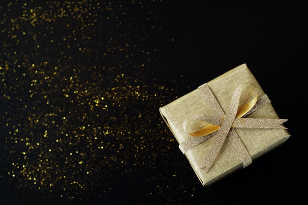 Contenitore di regalo avvolto dorato su fondo nero.