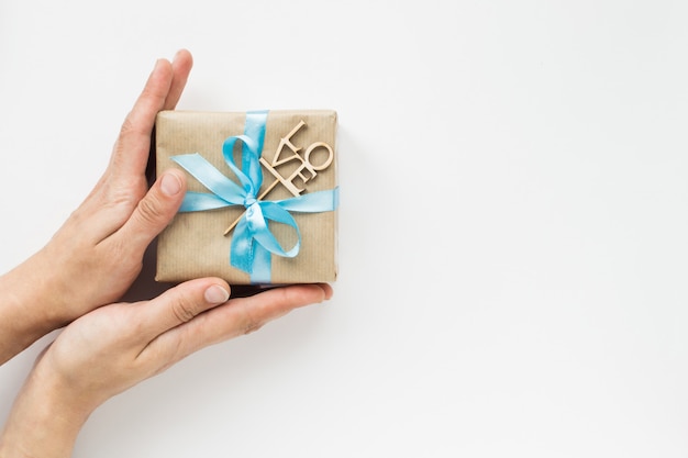 Contenitore di regalo avvolto in carta marrone con il nastro blu in mani della donna su bianco